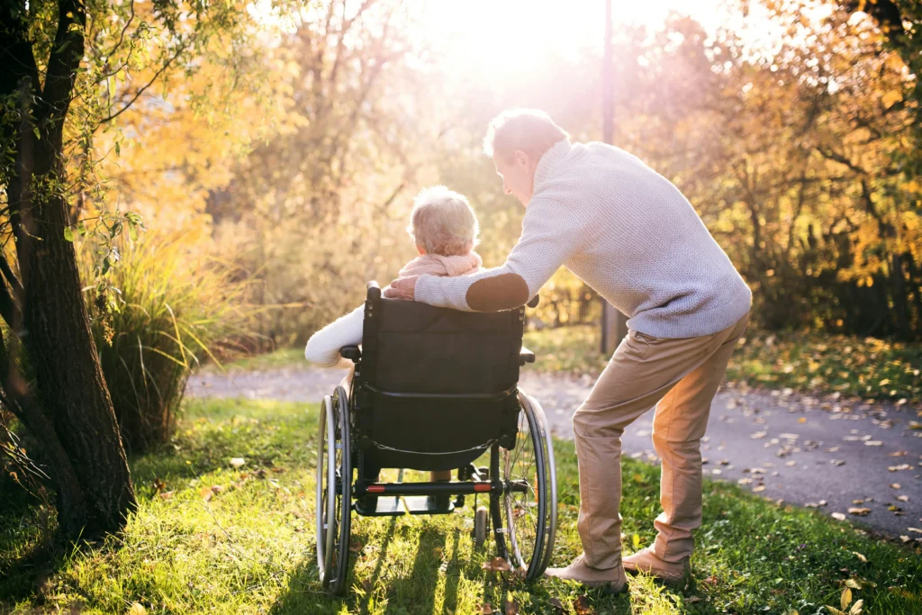 Carer pushing an older person in a wheelchair along a sunny garden path.